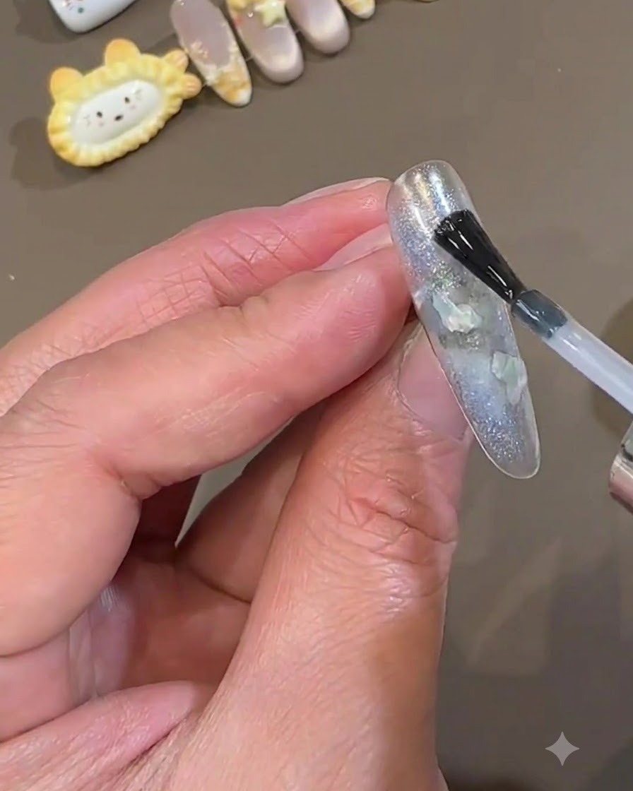Un pennello da smalto applica un sottile strato liscio di top coat trasparente su ununghia press-on azzurro ghiaccio incapsulata.