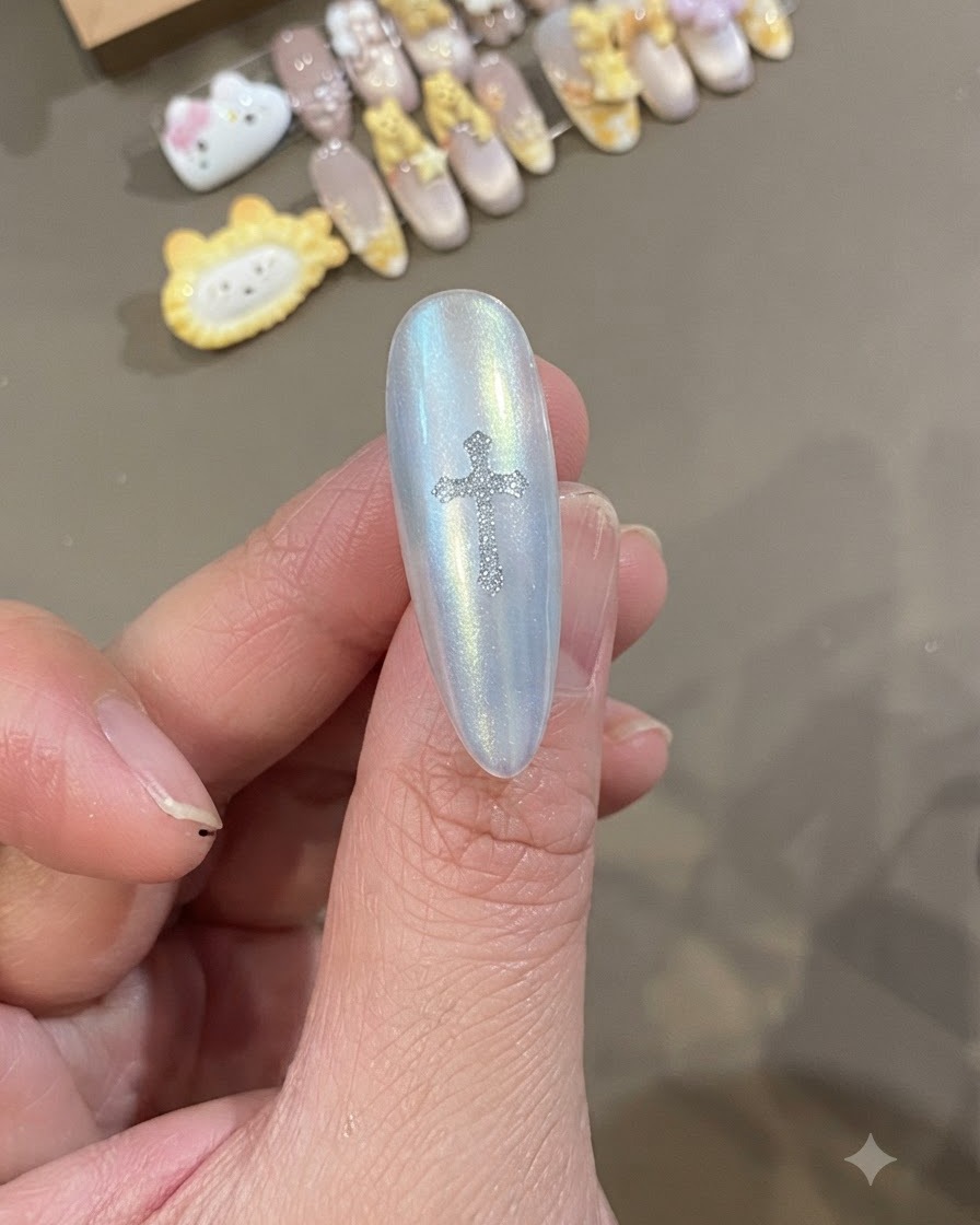 Primo piano di ununghia bianca perlescente con un adesivo a forma di croce Chrome Heart argentato e brillante posizionato esattamente al centro.