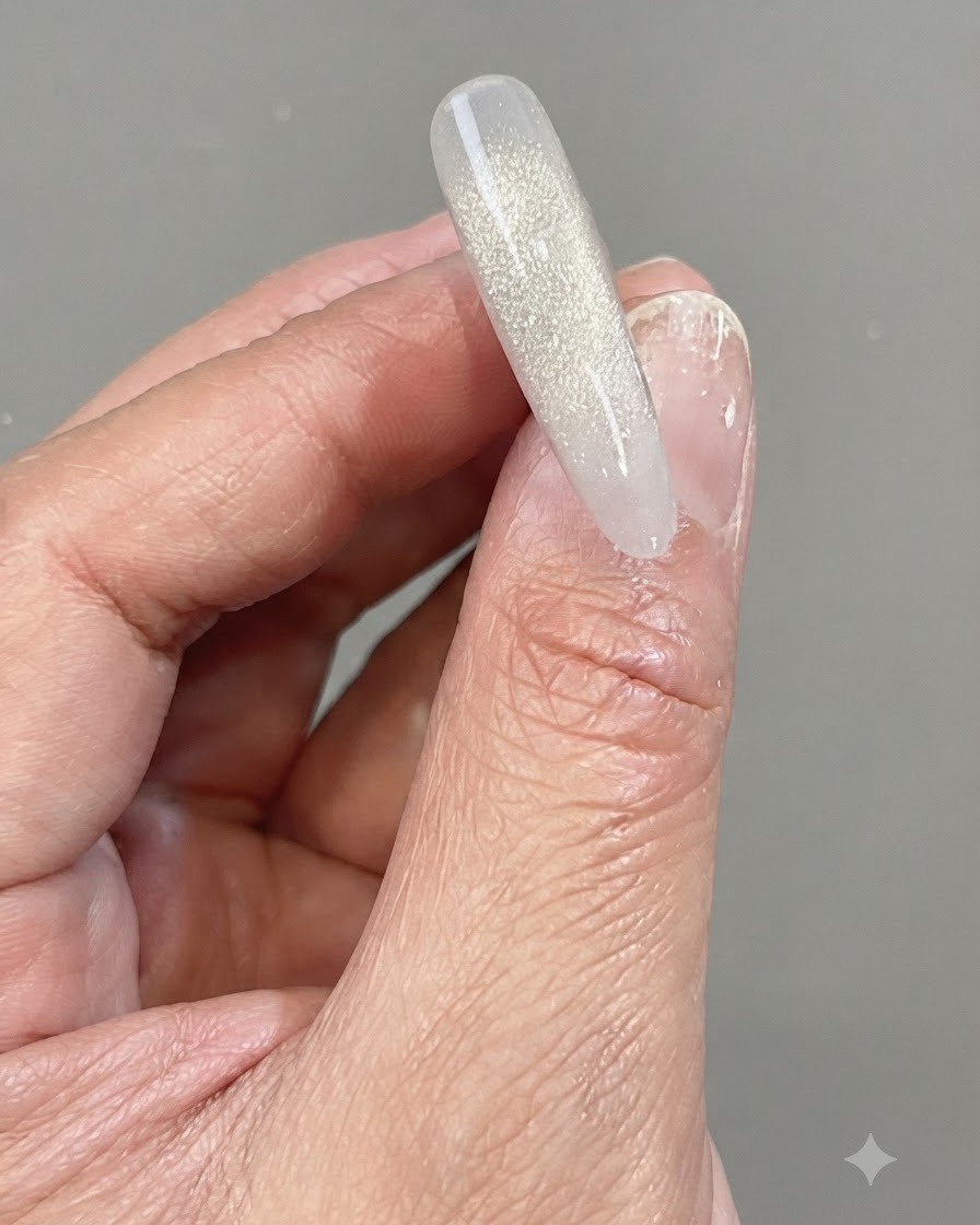 Una mano che tiene una punta dunghia trasparente con una sfumatura verticale e scintillante fatta di gel diamantato frantumato riflettente.