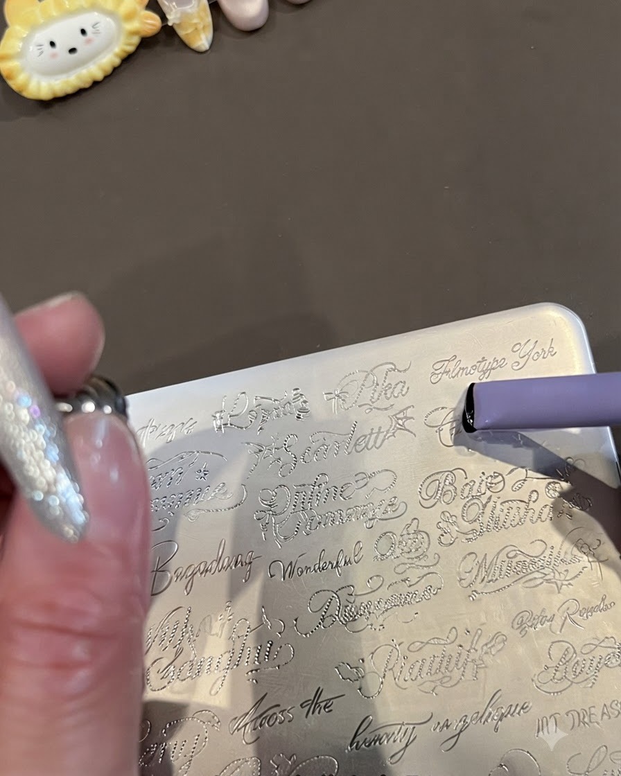 Primo piano di una piastra di stampa in metallo incisa con parole corsive in inglese e un timbro in gelatina viola che raccoglie il design.
