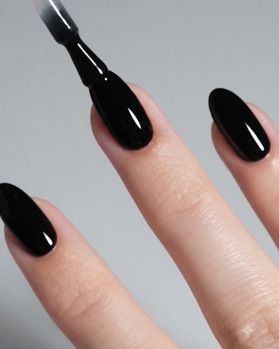 Un primo piano di un pennello che applica uno smalto gel nero lucido su ununghia a mandorla.