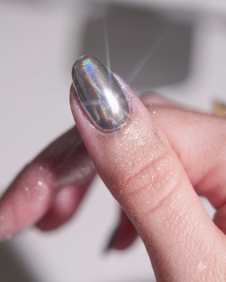 Un dito con una base in gel nero polimerizzata mentre viene strofinata con una polvere cromata argentata usando un applicatore in spugna di silicone.