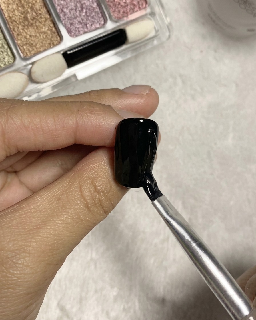 Pennello a punta divisa che traccia linee verticali testurizzate usando colla trasparente sulla superficie di ununghia in gel nero.