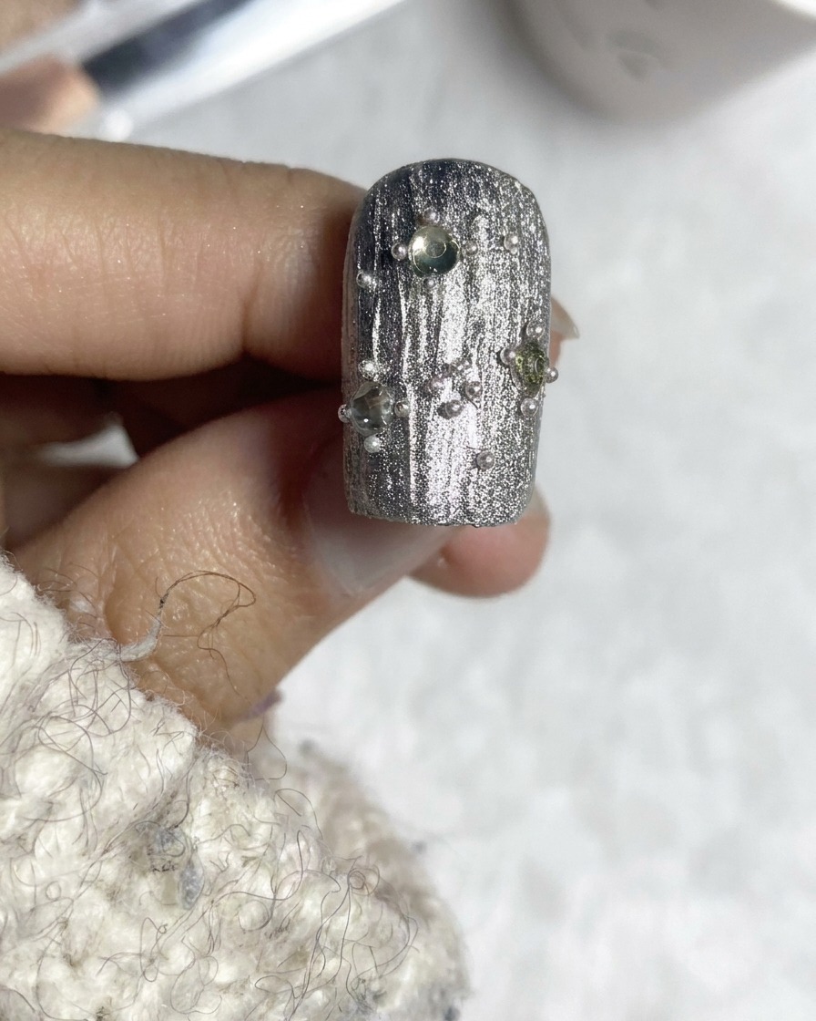 Un pennello per top coat che rifinisce un design per unghie testurizzato in argento decorato.