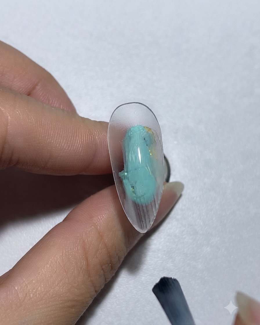 Un pennello che applica gel colorato verde-azzurro su ununghia.