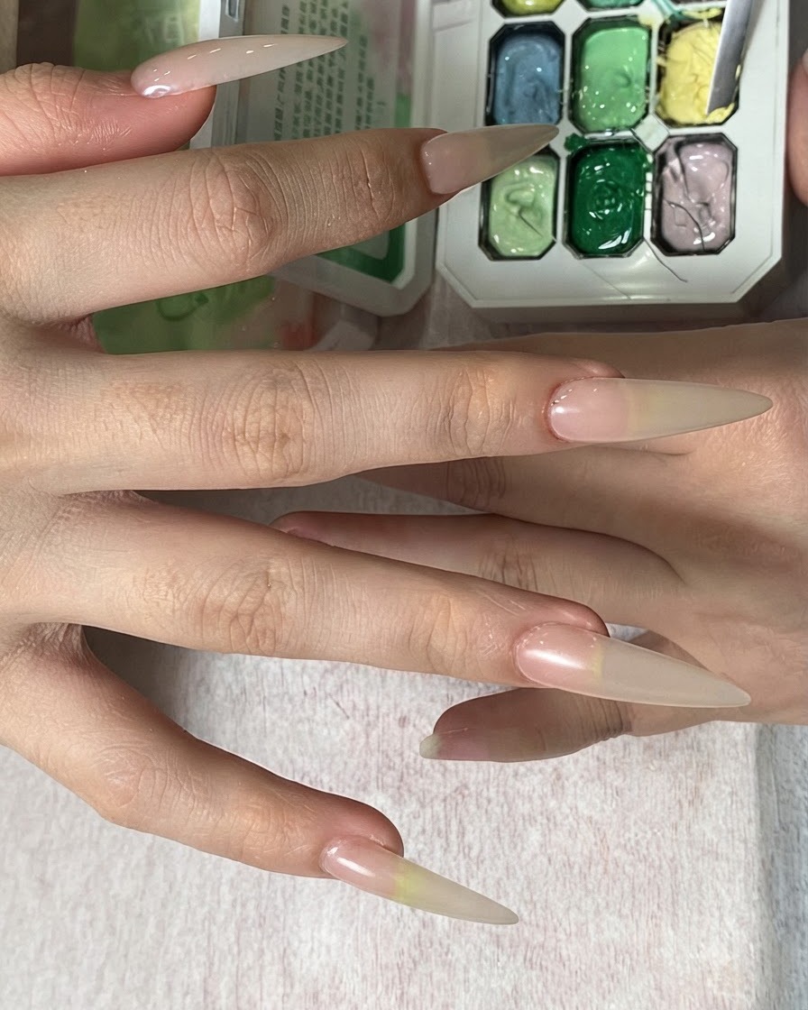 Una mano che regge una spugnetta sopra una tavolozza di colori, tamponando il colore giallo sulla punta di ununghia lunga.
