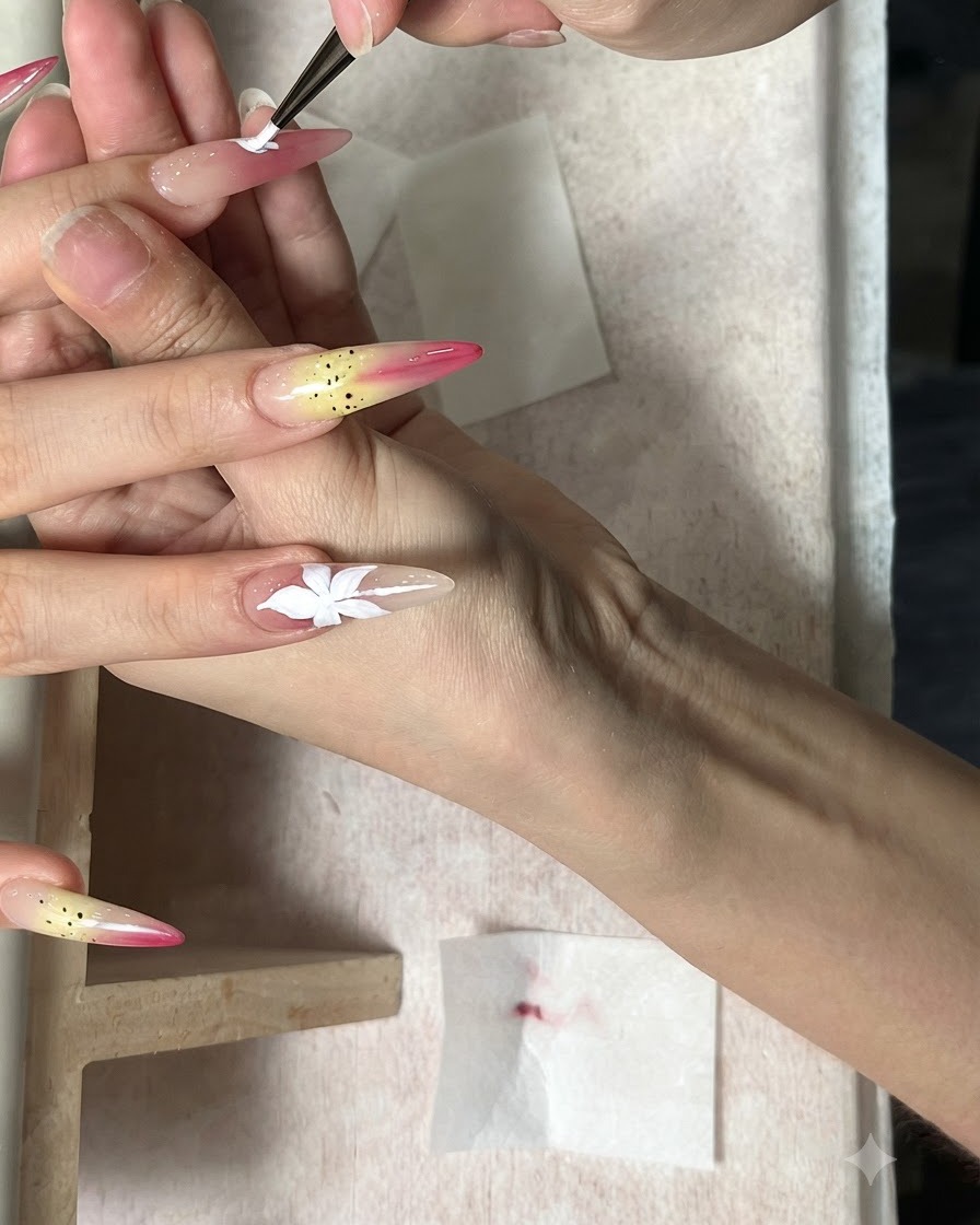 Un pennello fine che dipinge un fiore bianco a cinque petali su ununghia nude allungata.