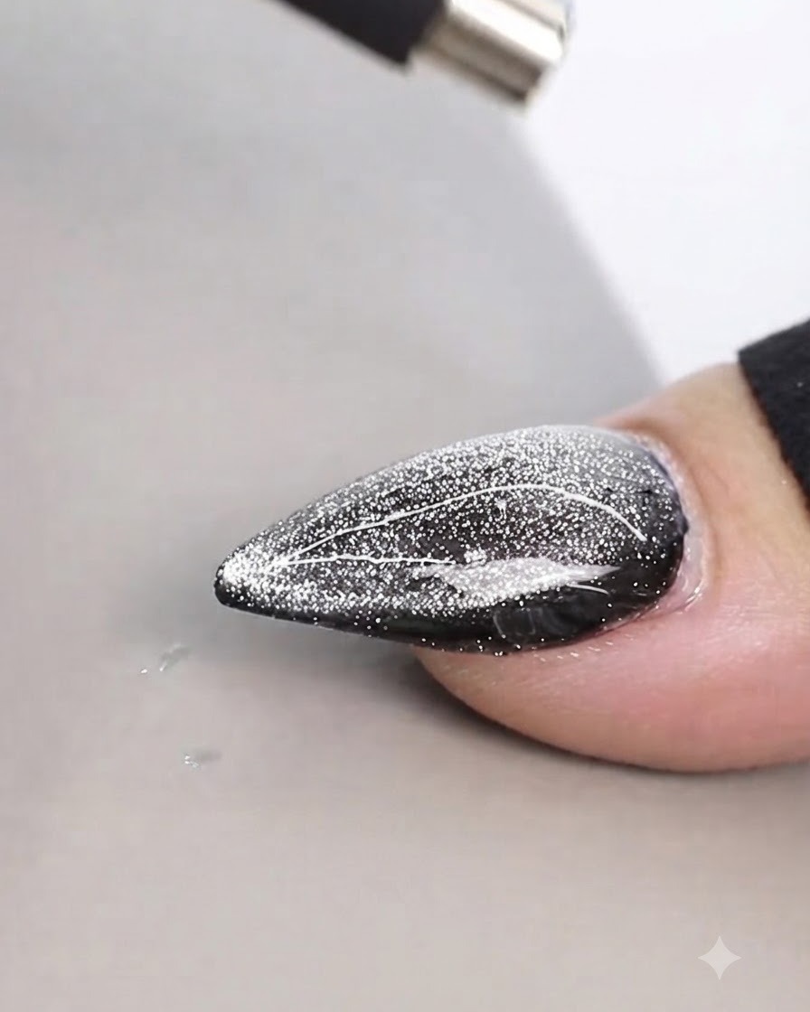 Uno strumento magnetico cilindrico tenuto da vicino sopra un design di unghie cat eye brillante per creare linee sottili.
