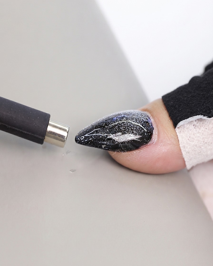 Uno strumento magnetico nero a forma di penna avvicinato a una superficie testurizzata di ununghia cat eye.