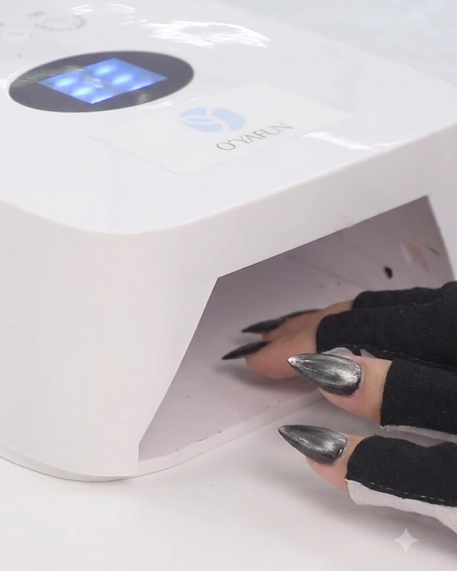 Una mano con guanti neri senza dita che posiziona le dita allinterno di una lampada per unghie UV LED bianca per polimerizzare lo smalto gel.