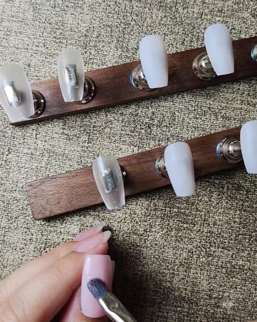 Un pennello piatto da gel che applica un secondo strato di smalto gel rosa nude semitrasparente sullunghia.