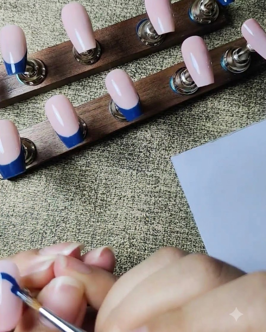 Un pennello liner sottile che disegna il contorno di una French blu scuro su ununghia posticcia rosa nude.