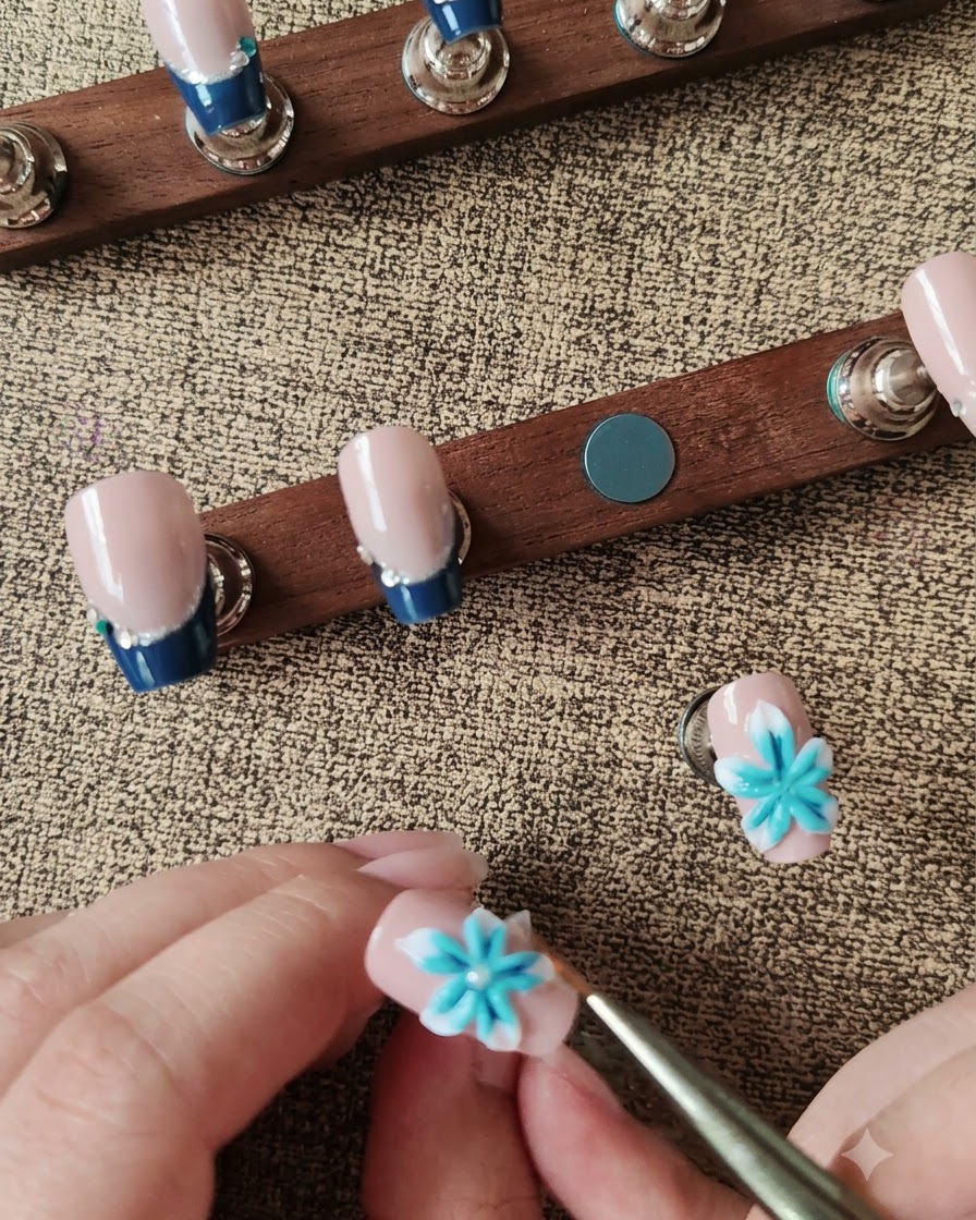 Una penna con cera che posiziona una perla bianca al centro di un fiore 3D blu e bianco.