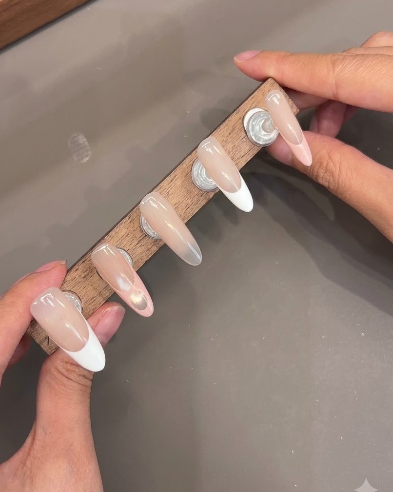 Più unghie press-on montate su un supporto di legno che mostrano strati di top coat lucido.