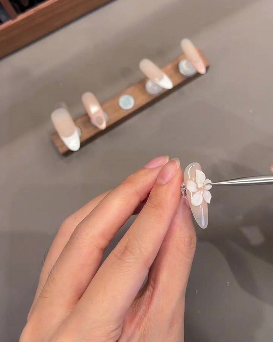 Un primo piano di uno strumento sottile che aggiunge un piccolo centro in gel bianco a un fiore 3D scolpito su ununghia.