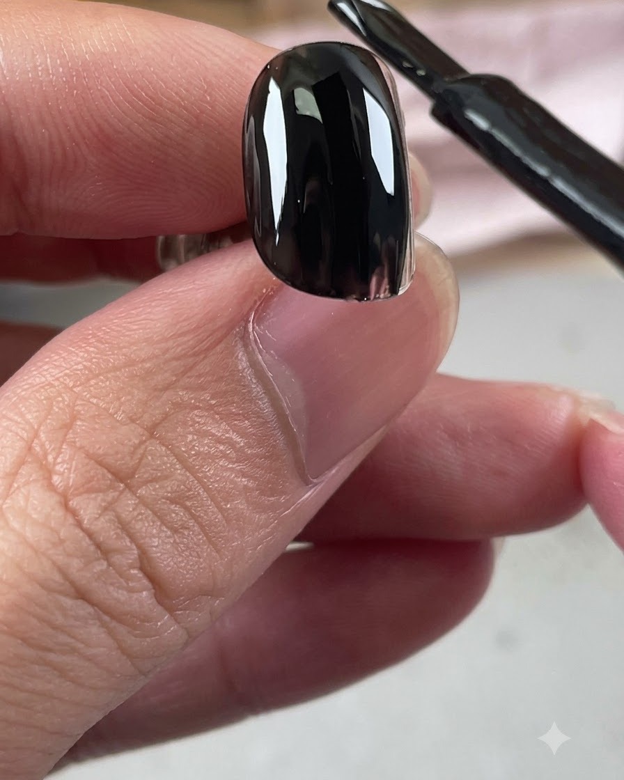 Un pennellino di smalto gel nero che applica uno strato lucido di base nera su ununghia.