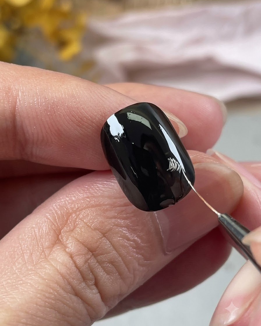 Vista ravvicinata di una mano che usa un pennello da nail art per tracciare i contorni argentati dei petali su ununghia nera.