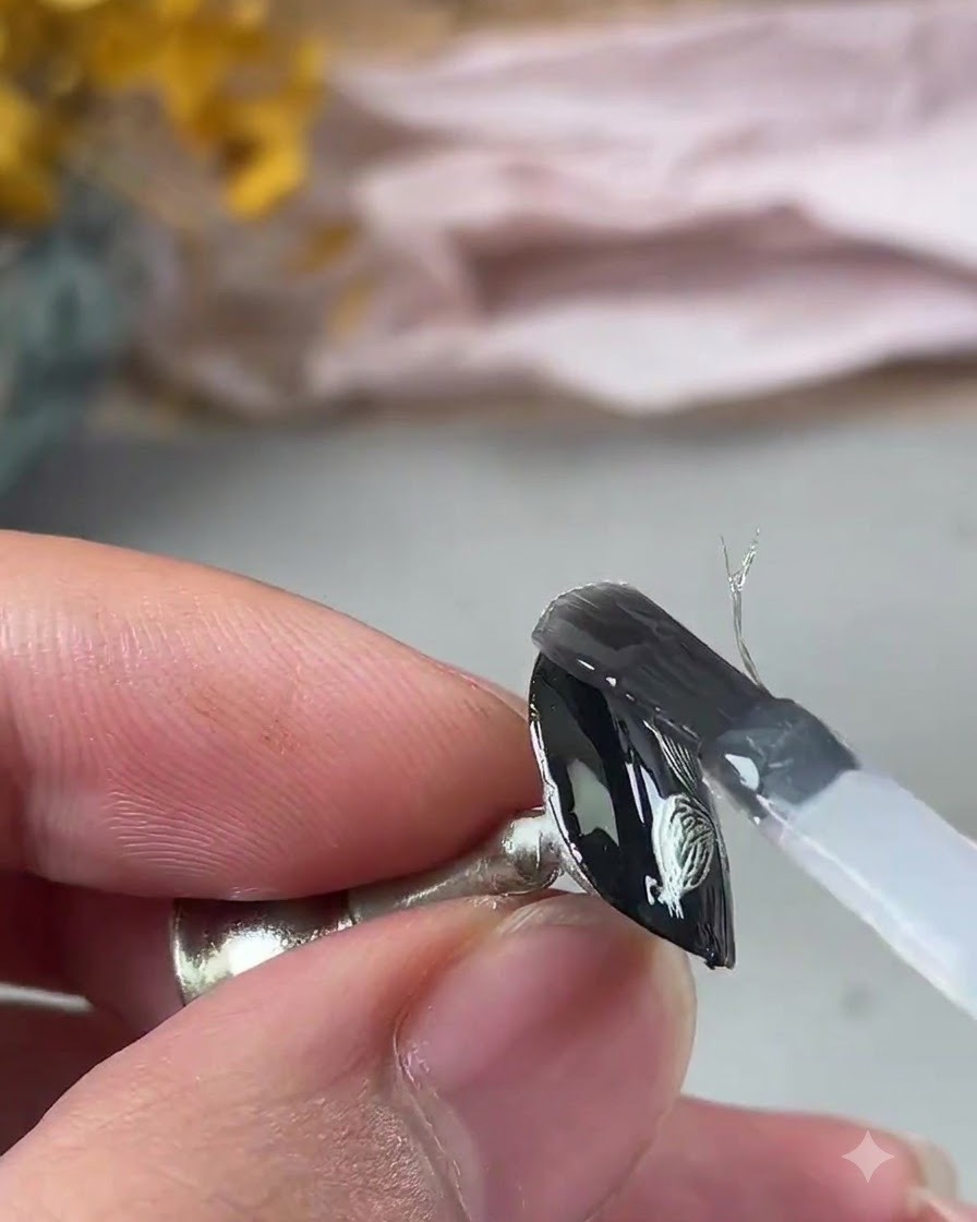 Un pennello che applica un gel rinforzante trasparente sulla nail art metallizzata testurizzata.