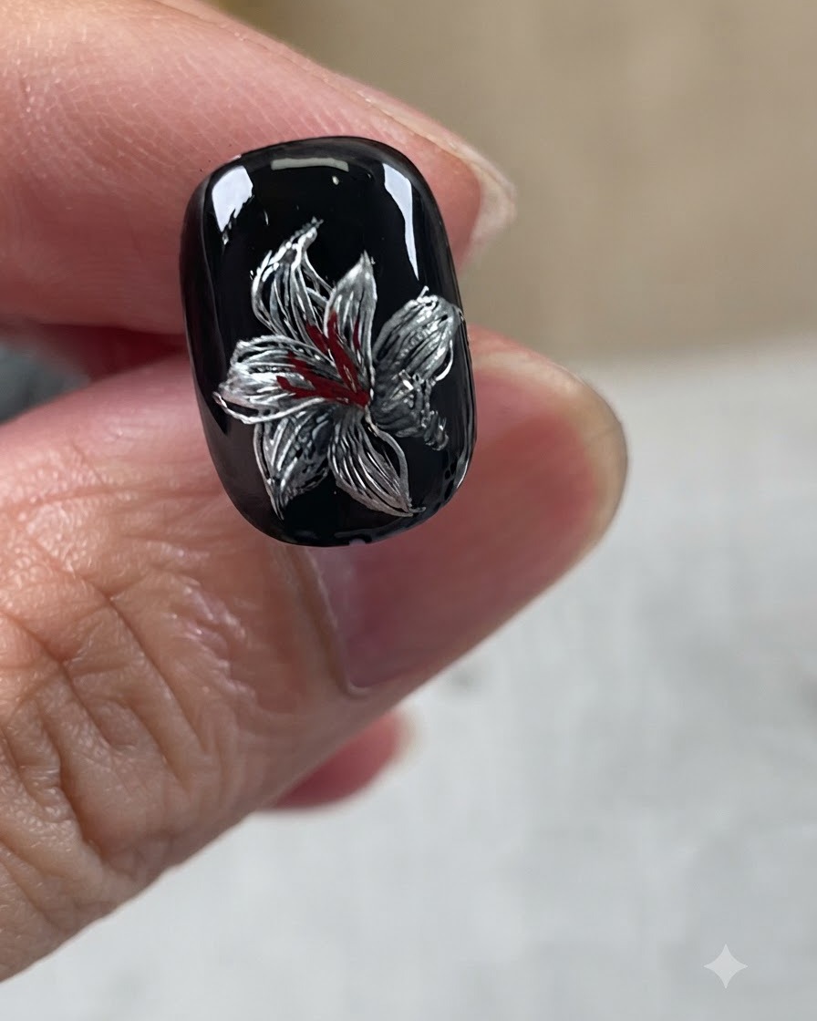 La nail art completata con base nera, petali in argento, tocchi bianchi e centro rosso.