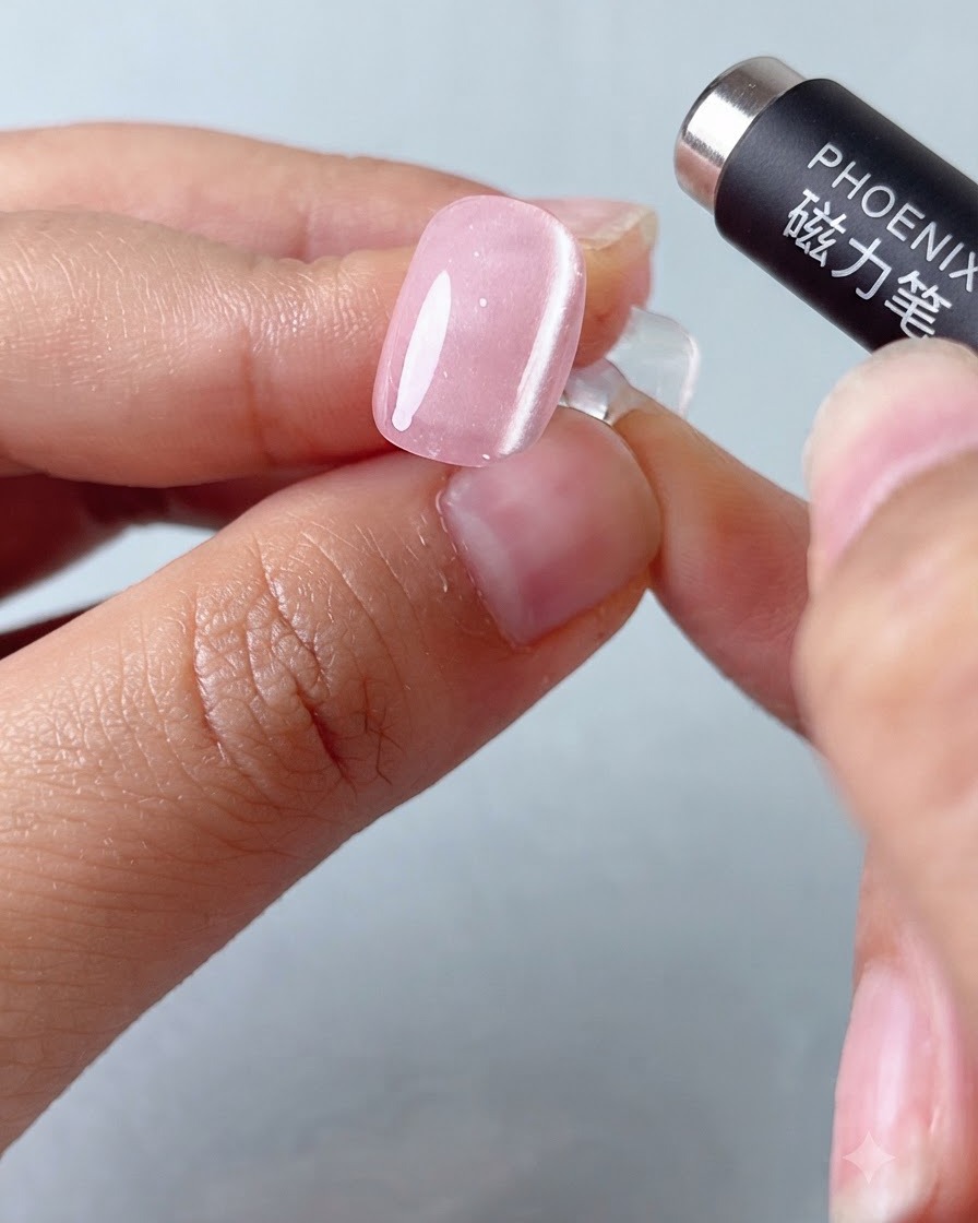 Un instrument magnetic tip stilou care planează deasupra unei unghii cu gel cat-eye roz pentru a modela banda de lumină.