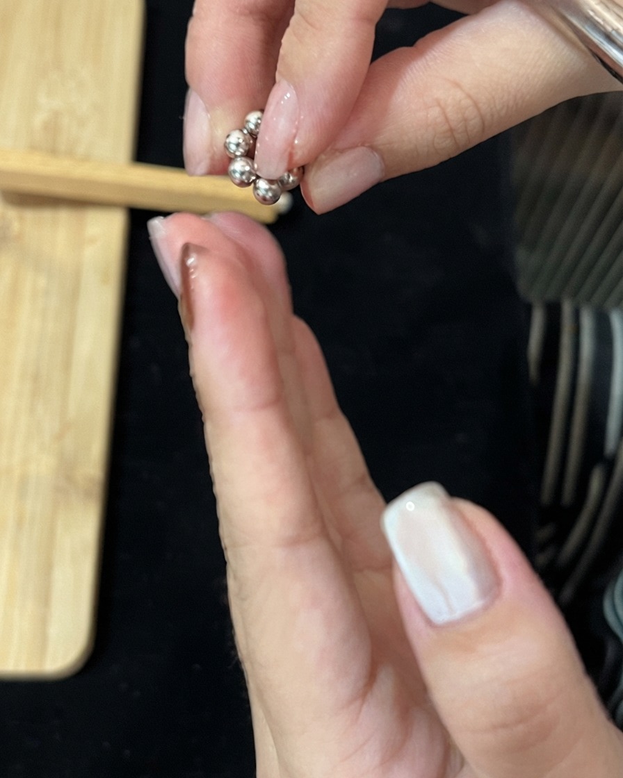Dita che tengono un piccolo gruppo circolare di sfere magnetiche metalliche sopra una mano.