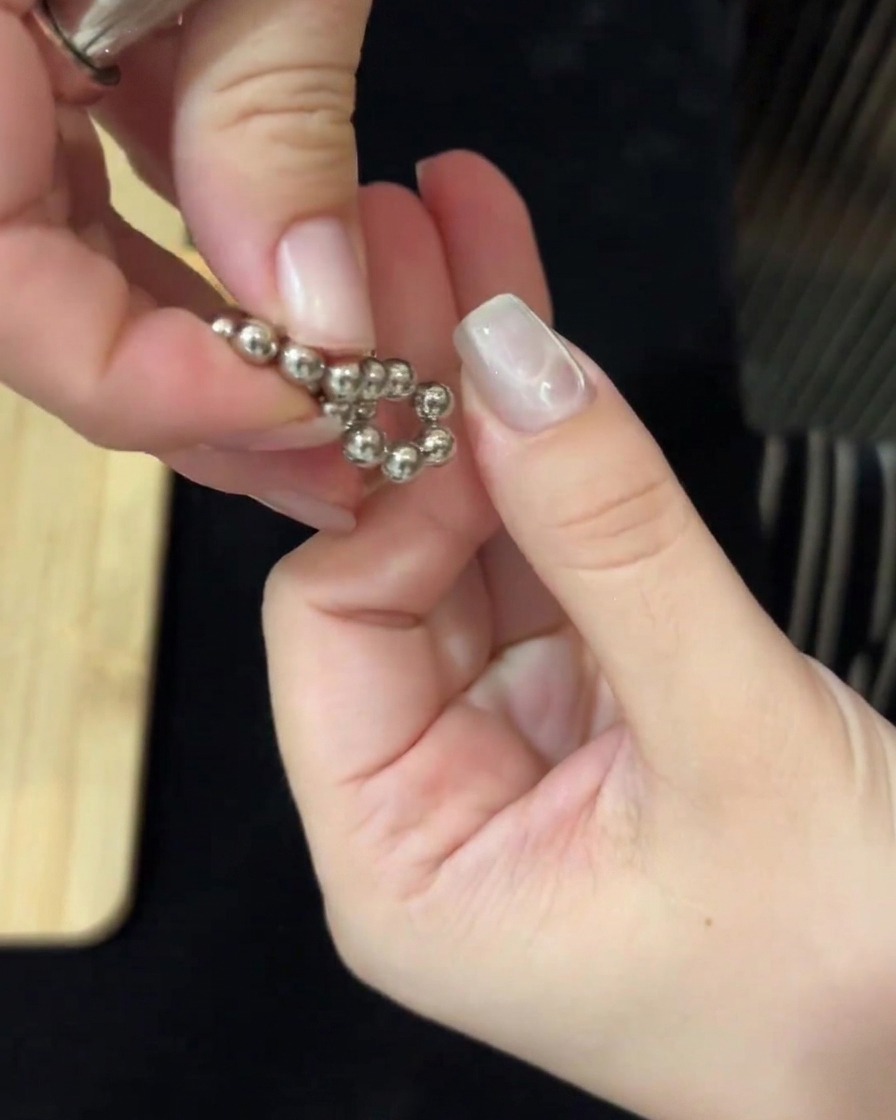 Mani che utilizzano strumenti magnetici su entrambi i lati per manipolare le sfere metalliche e creare increspature sullunghia.