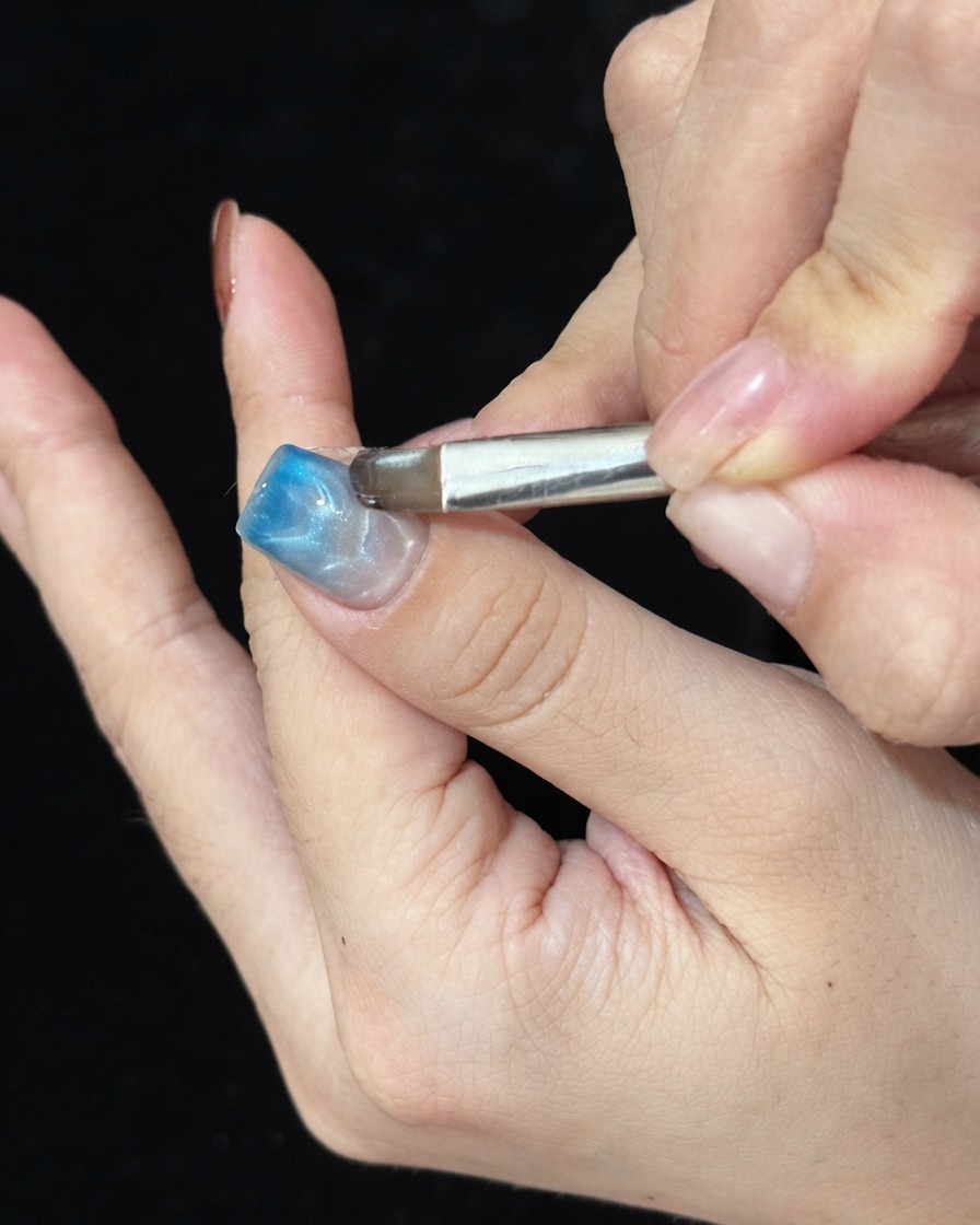 Un pennello che tampona il gel vetro blu sulla punta di ununghia curata per definire il gradiente.
