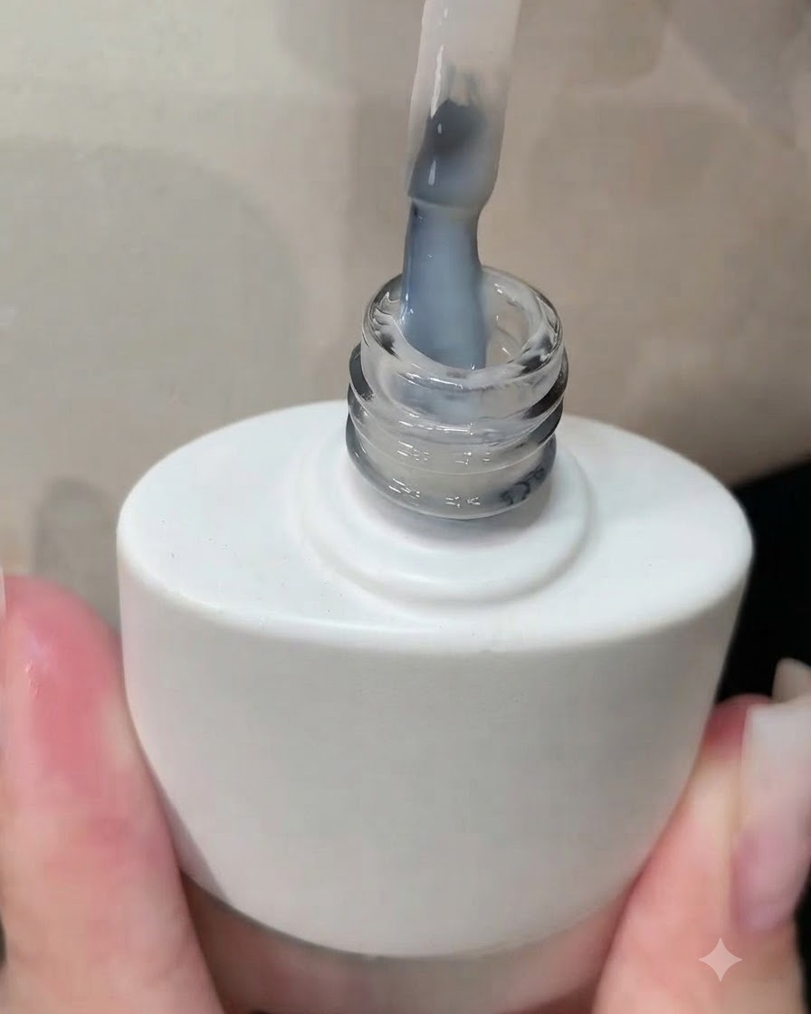 Un pennello che solleva una bottiglia di smalto gel bianco con un rivestimento bianco latte visibile sulle setole.