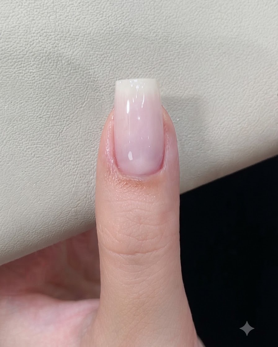 Ununghia con una base in gel bianco latte polimerizzata sotto una lampada per unghie.
