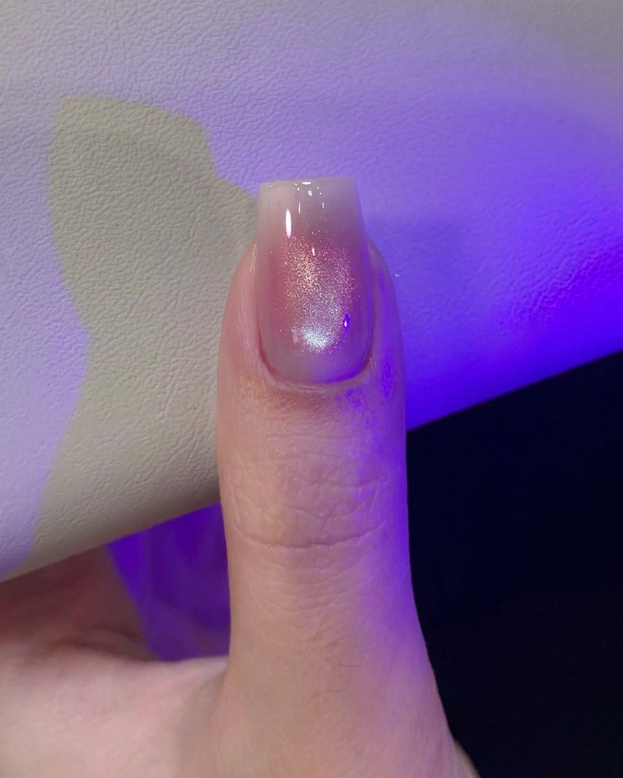Un pollice sotto la luce viola della lampada UV/LED che polimerizza il design per unghie cat-eye appena magnetizzato.