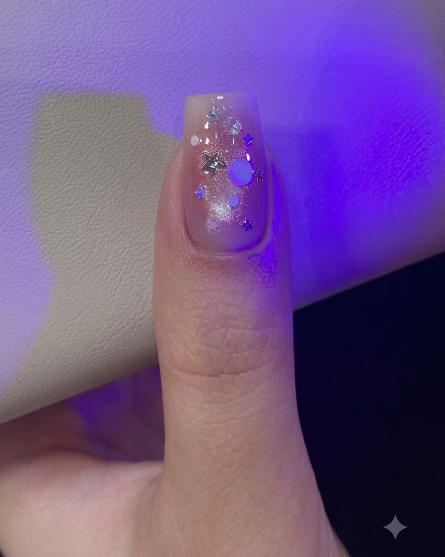 Un pollice sotto la luce della lampada decorato con paillettes glitterate iridescenti a stella e rotonde sparse.