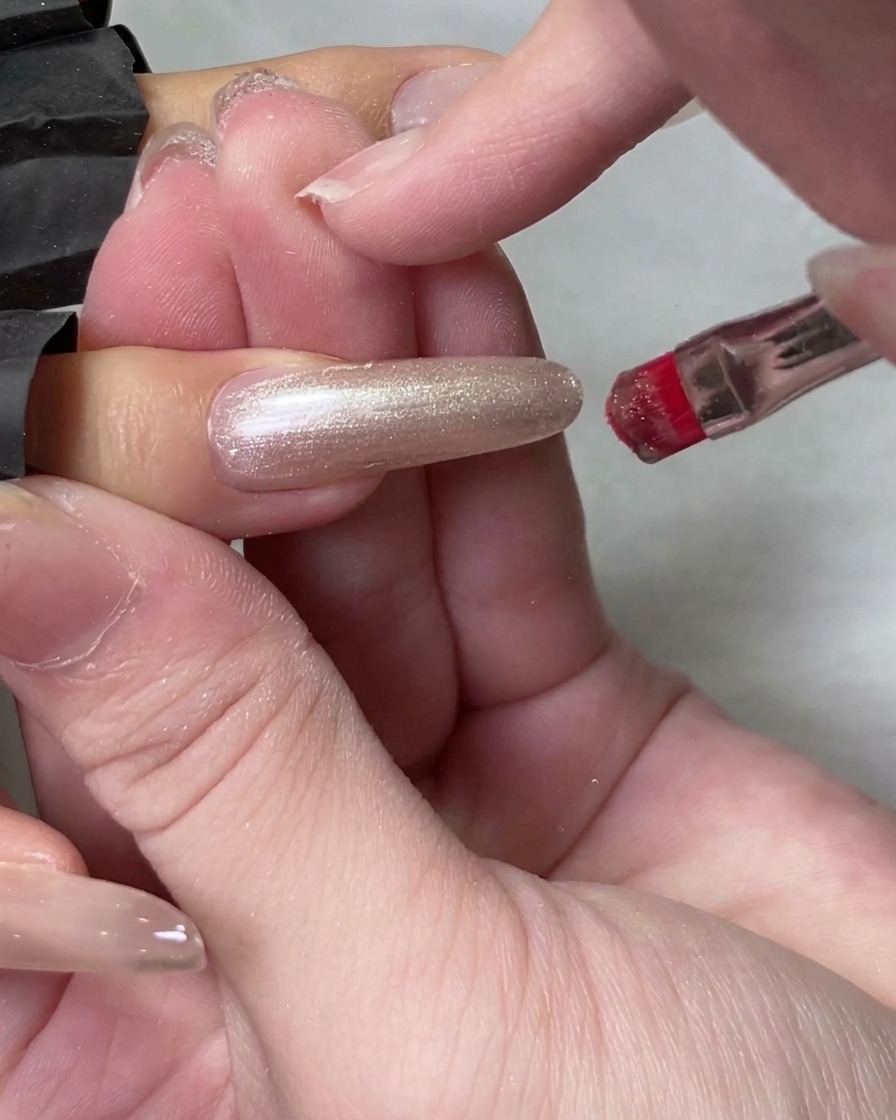 Un pennellino applica del gel cat eye traslucido su ununghia naturale lunga.
