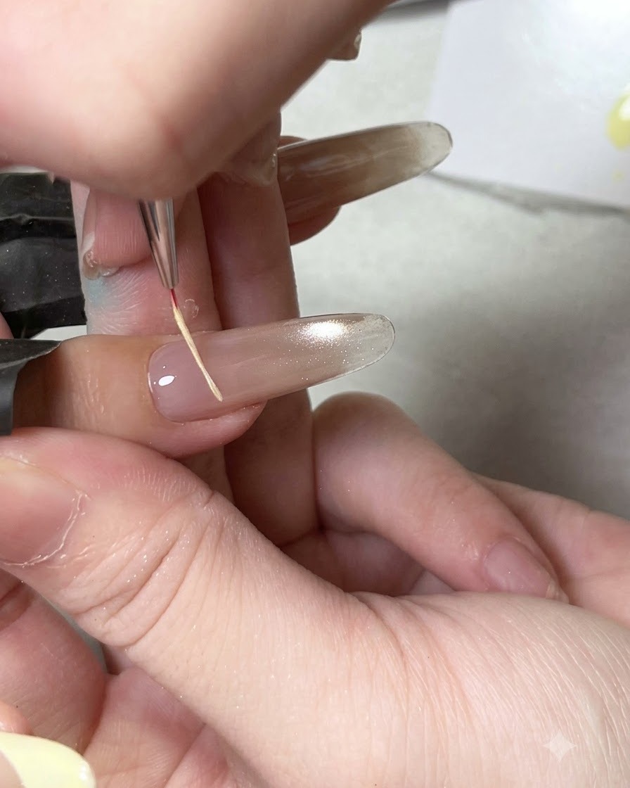 Un pennello di precisione applica il top coat lucido su una base per unghie cat eye polimerizzata.