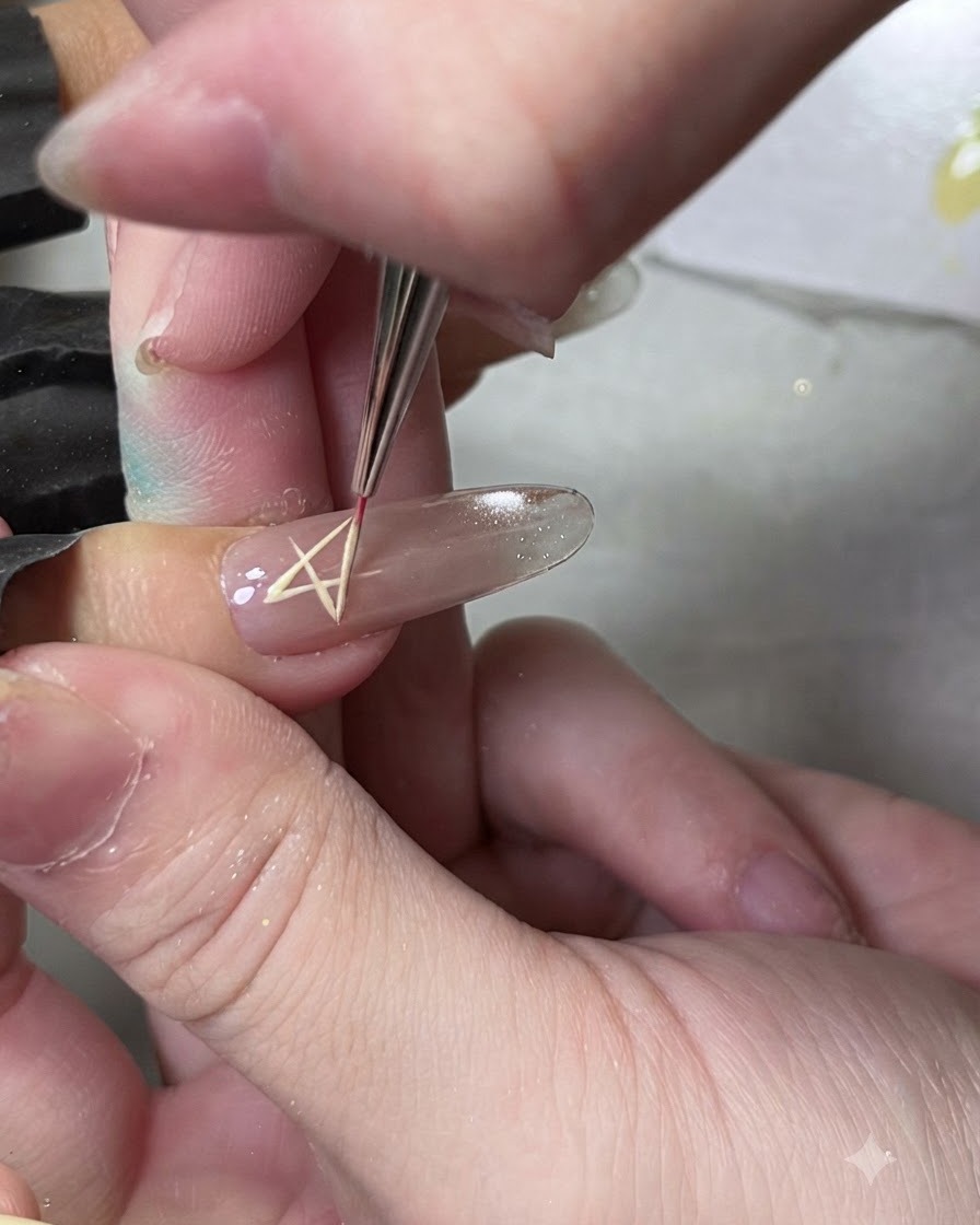Un pennello fine da linee disegna il contorno di una forma a stella su ununghia usando del gel giallo.
