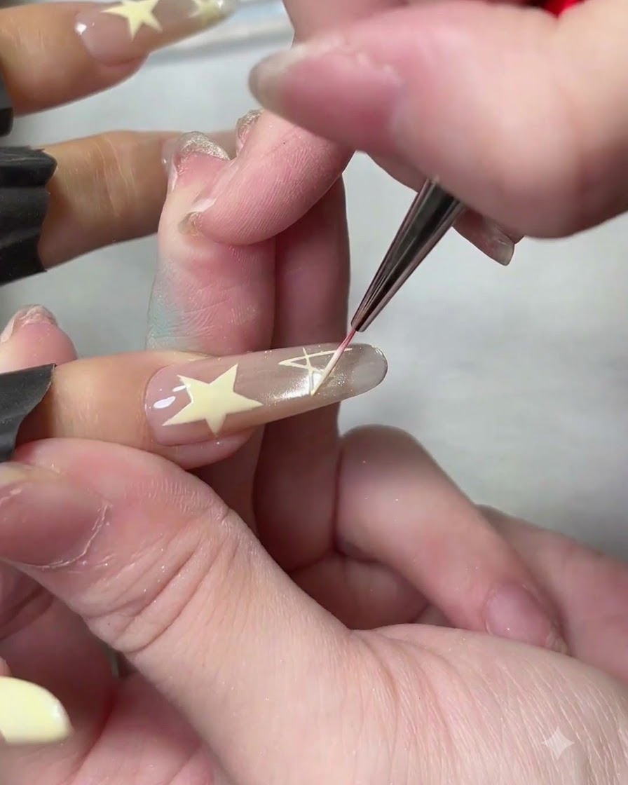 Un pennello liner sottile disegna il design di una stella bianca piena su ununghia artificiale dai toni neutri.