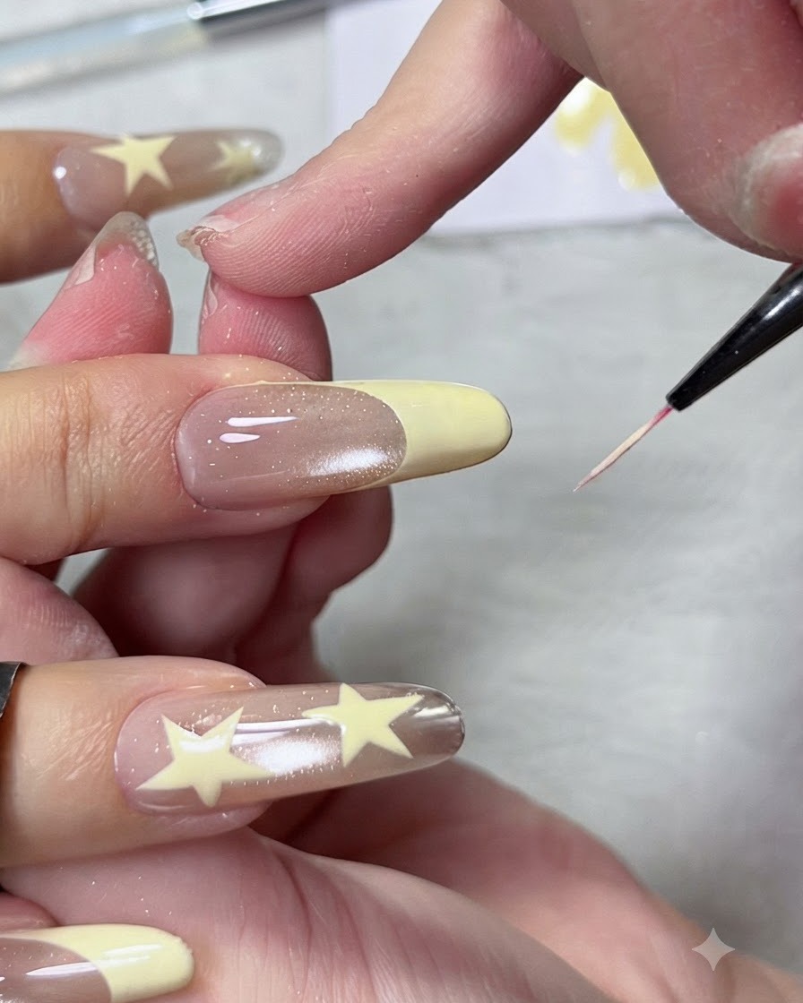 Primo piano di un pennello liner sottile che modella e affina la linea del sorriso di una punta french pastello su ununghia a mandorla lunga.