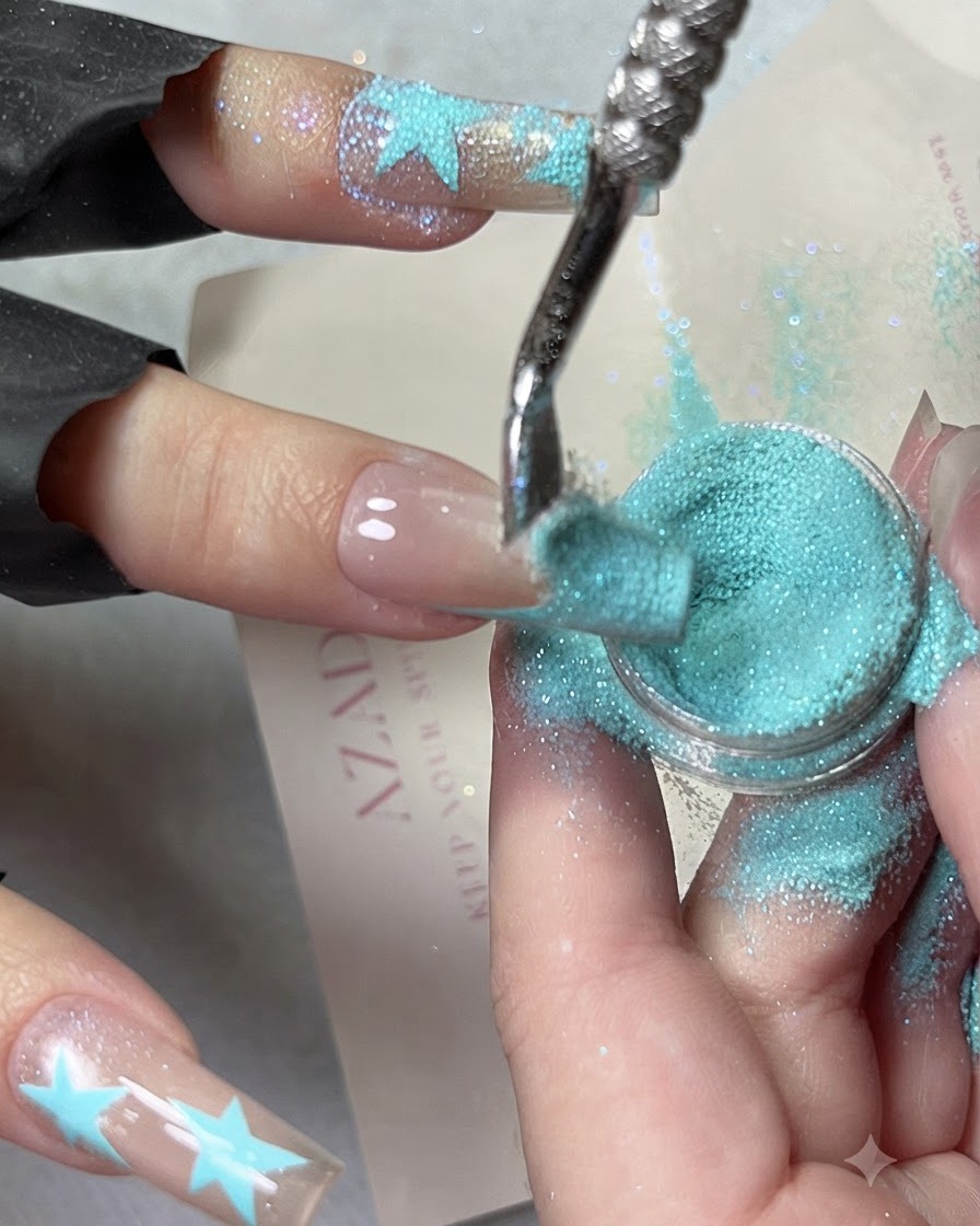 Immagine in primo piano che mostra la polvere di diamante frantumato azzurra fatta cadere a cascata su un design french tip blu.